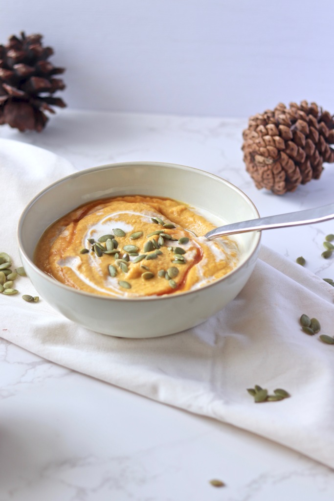 Creamy cauliflower pumpkin soup topped with pumpkin seeds a drizzle of maple syrup and cream
